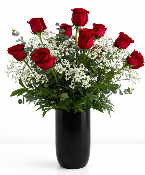 One dozen red roses and greenery in a clear glass vase.