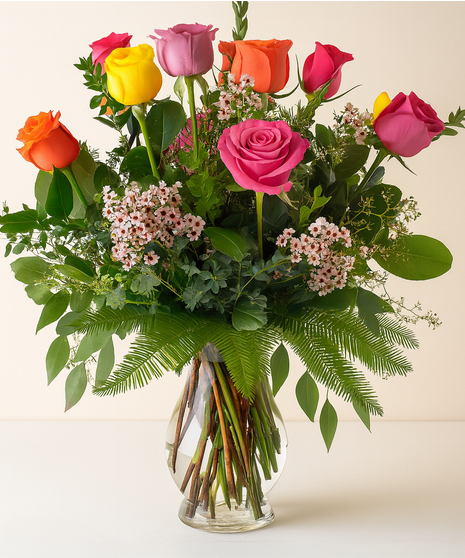 Roses in assorted colors in a glass vase with greenery and baby's breath.