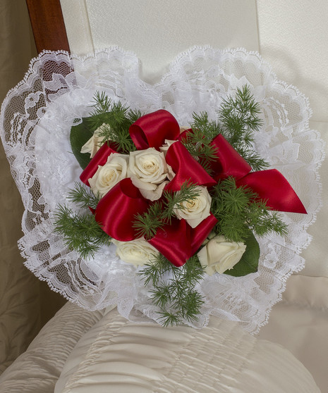 Satin pillow decorated with red and white roses, ribbon and greenery.