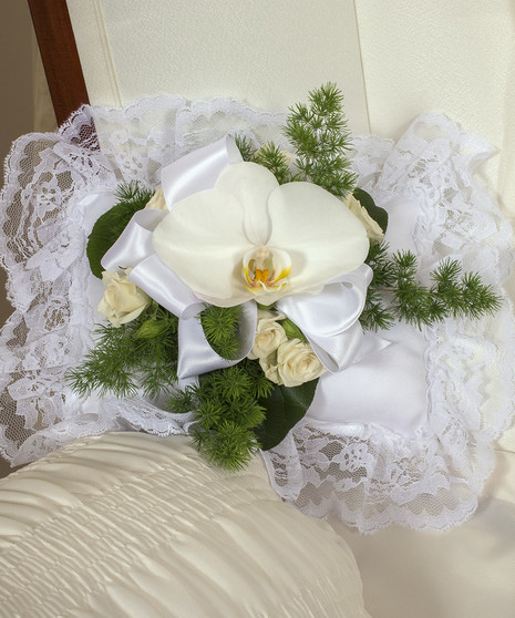 Casket pillow adorned with white orchids and greenery.