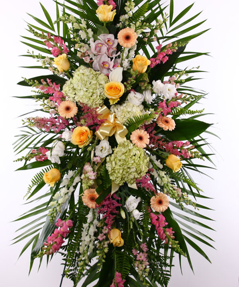 Sympathy spray of peach and yellow flowers with greenery displayed on an easel. 