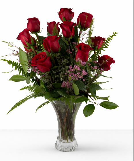 One dozen red roses and greenery in a clear glass vase.