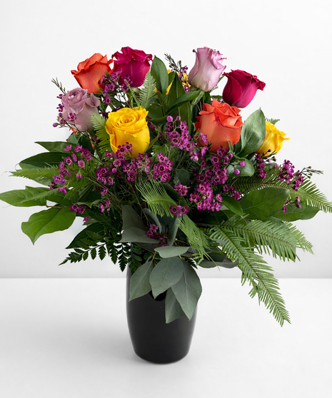 Roses in assorted colors in a glass vase with greenery and baby's breath.