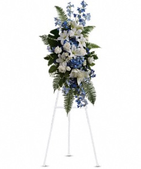 Sympathy spray of blue and white flowers and ferns presented on an easel. 