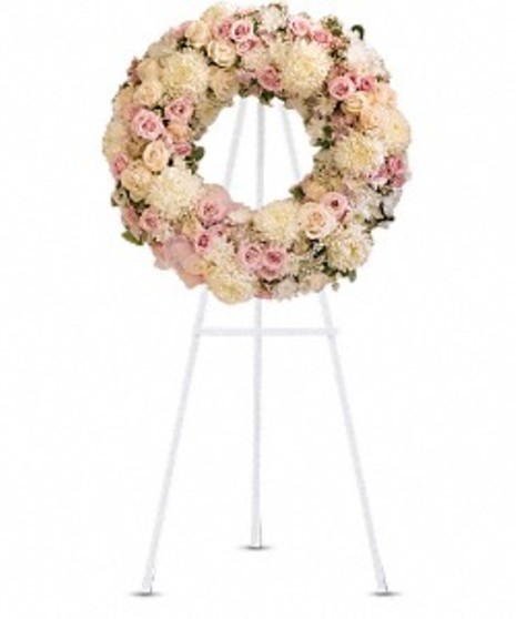 Sympathy wreath of pastel pink and white flowers displayed on an easel. 