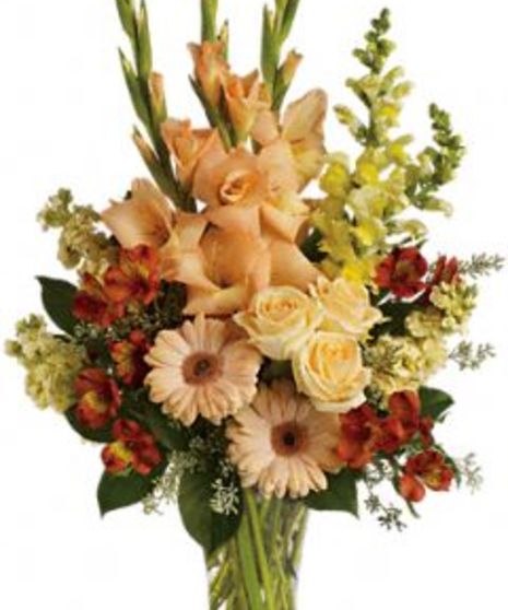 Sympathy arrangement with peach, orange and yellow flowers in a glass vase.