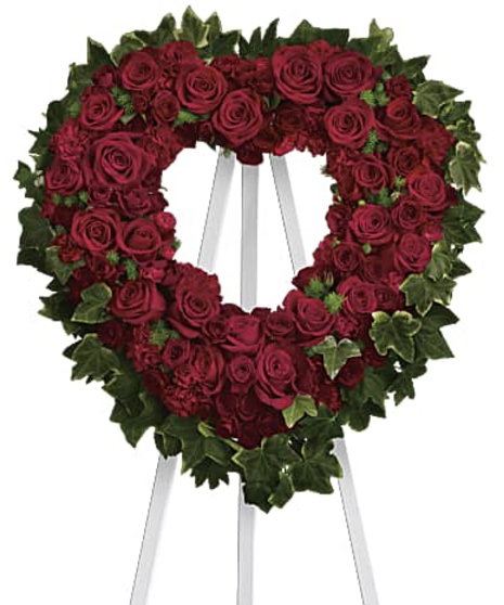 Sympathy heart wreath of red roses and greenery displayed on an easel. 